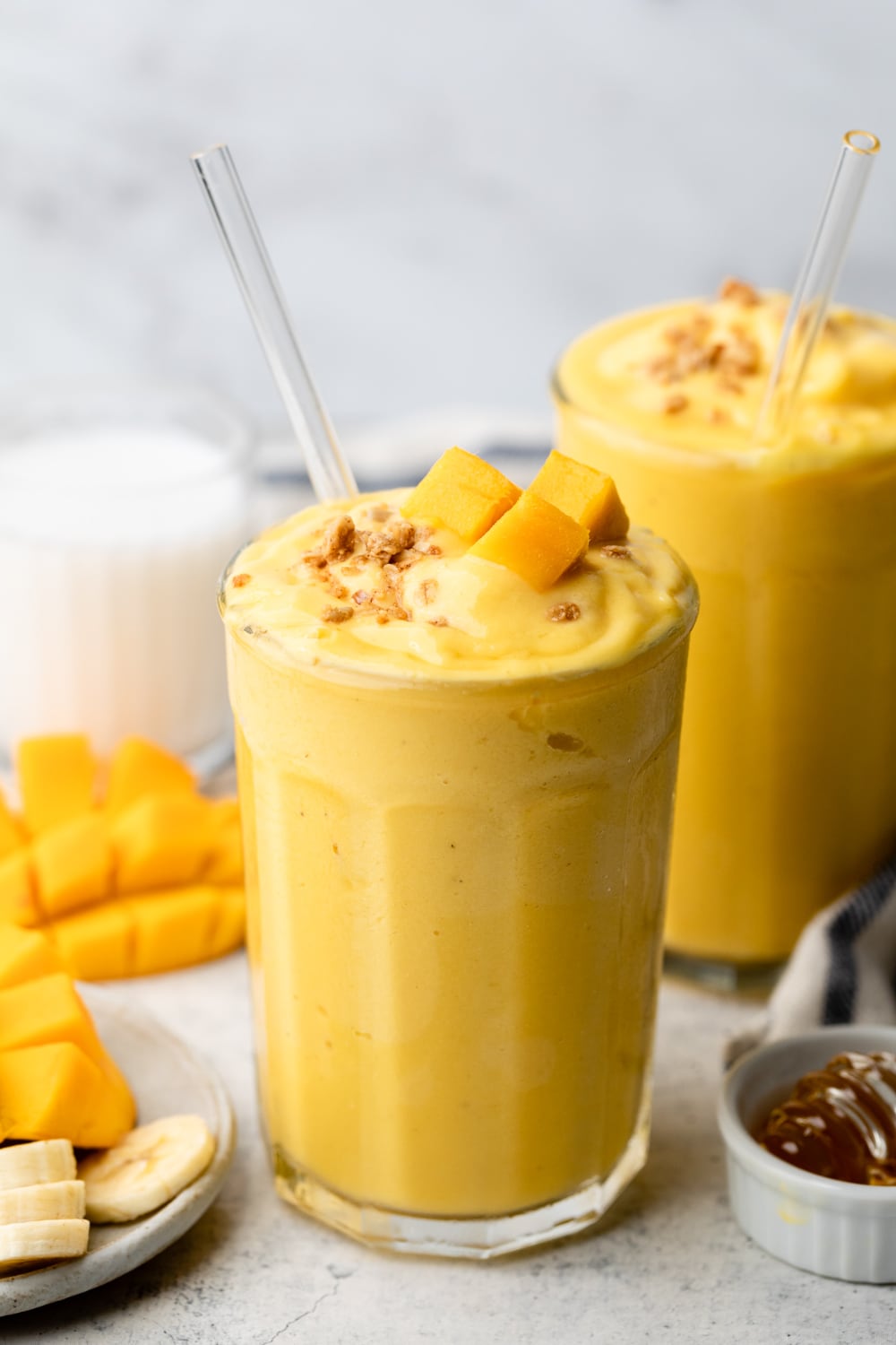 Two smoothies with a straw and mango on top. 