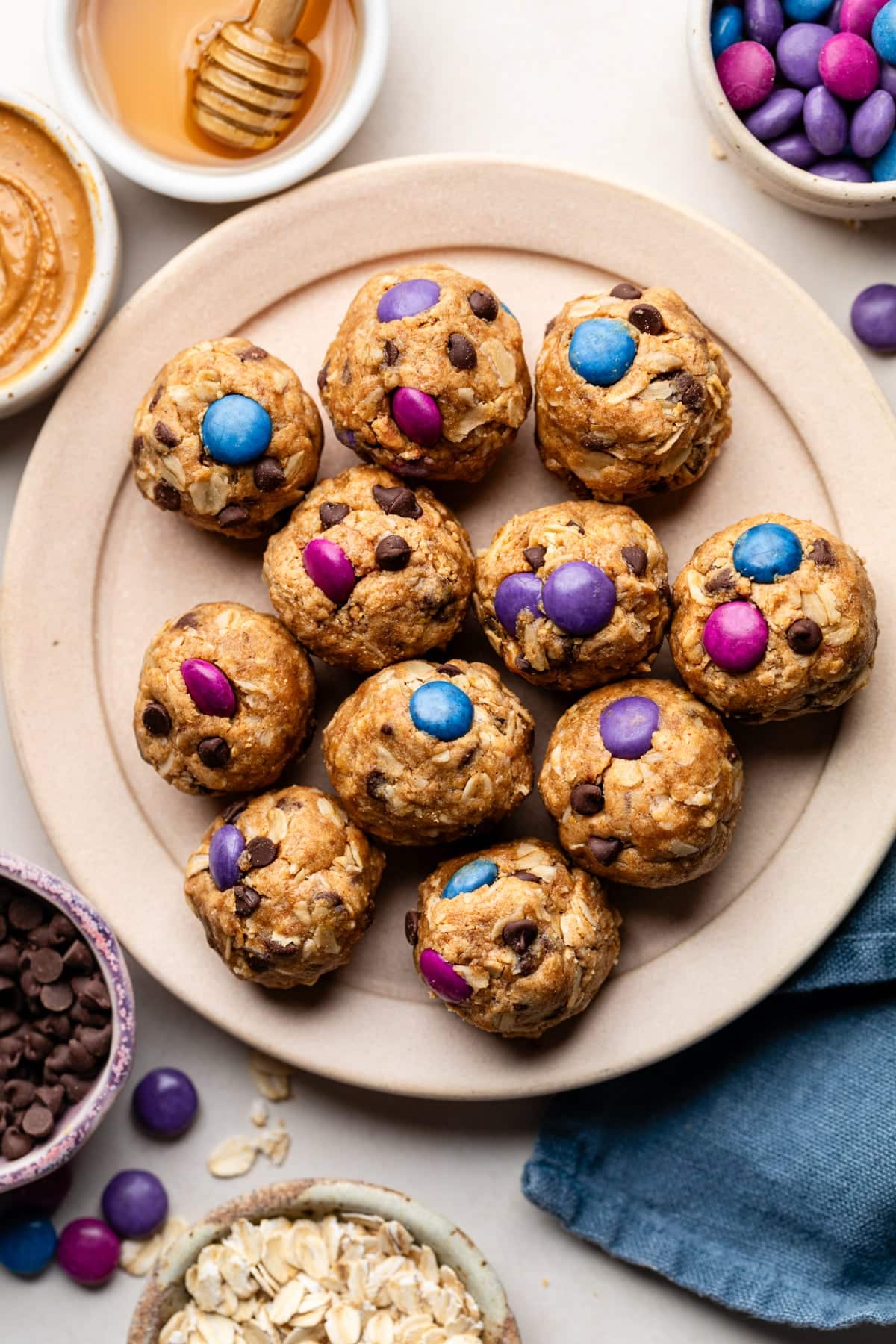 A plate of protein balls packed with all the ingredients of monster cookies, including rolled oats, peanut butter, chocolate, and candy pieces.