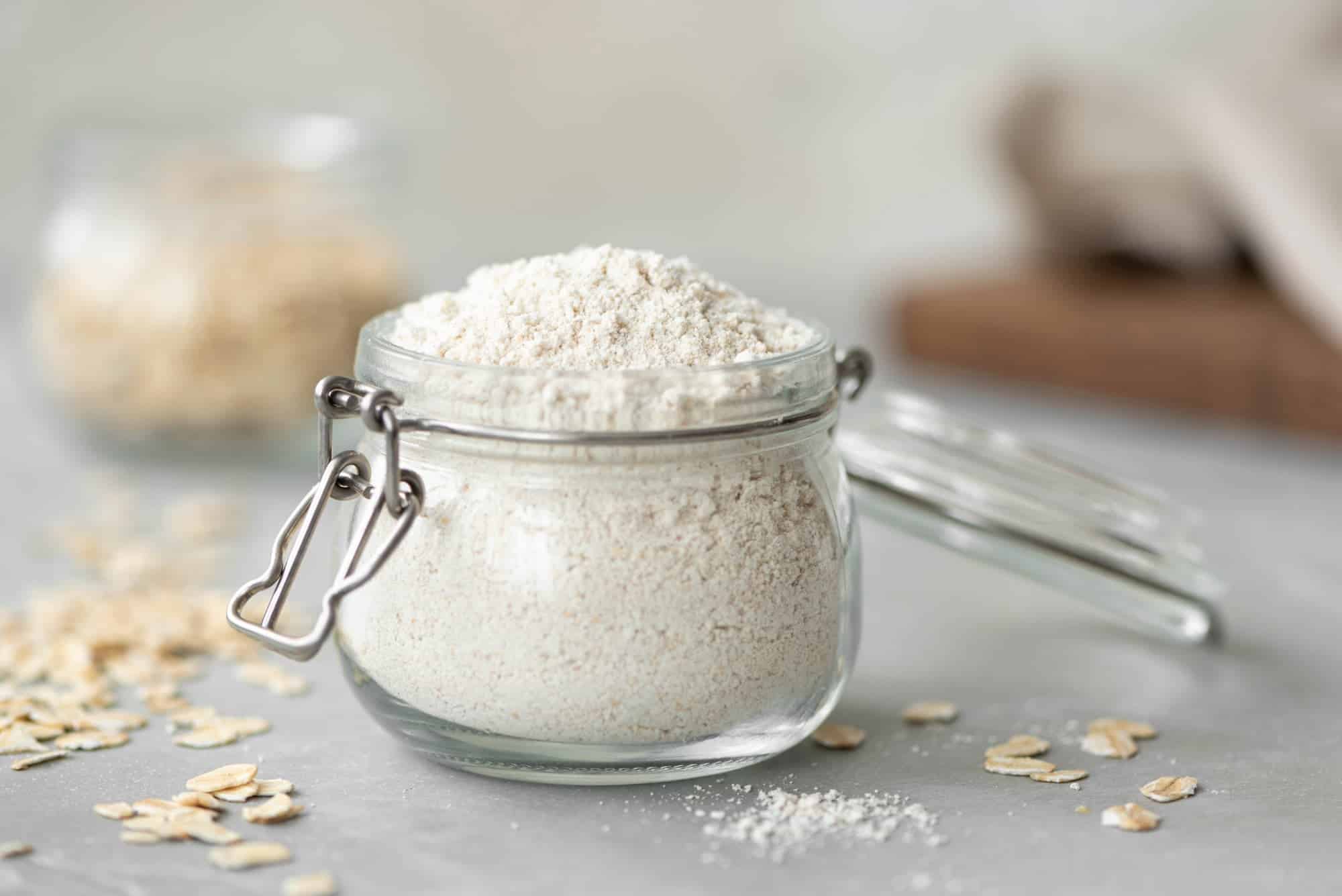 A jar of oat flour with oats surrounding it.