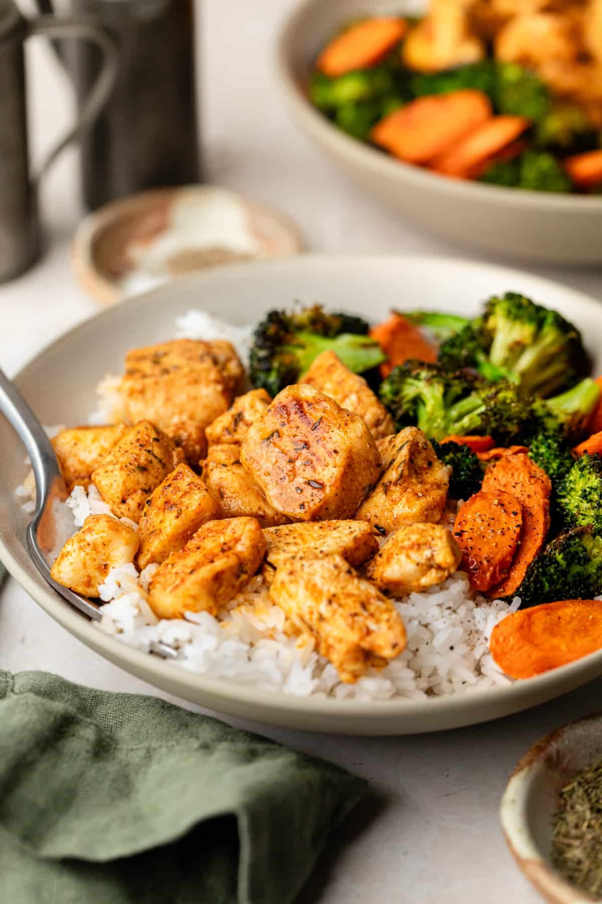 Oven baked chicken bites on a plate with a spoon served over rice and grilled vegetables.