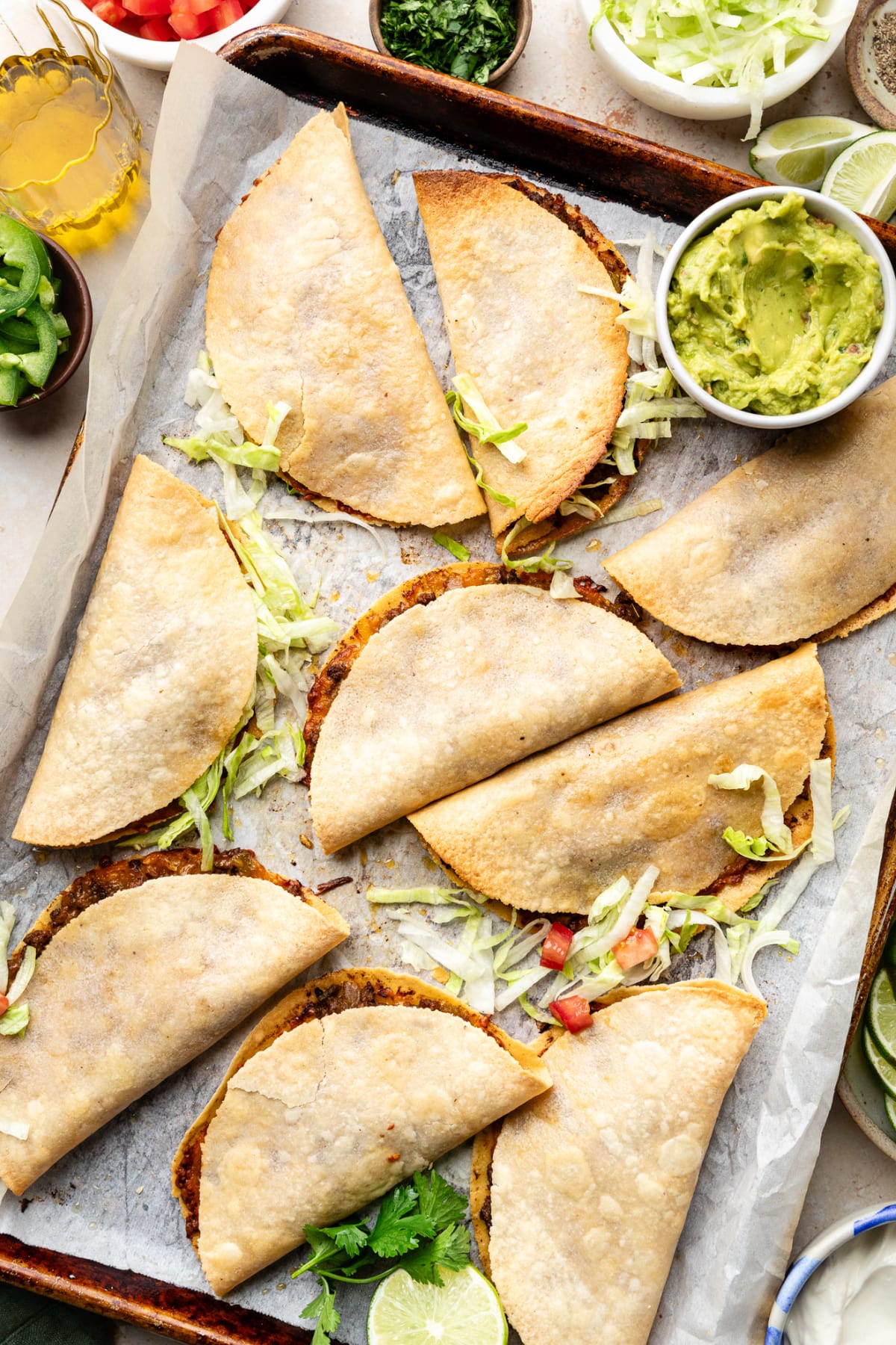 A sheet pan with the baked tacos fresh out of the oven with a few toppings, including shredded lettuce and onions.