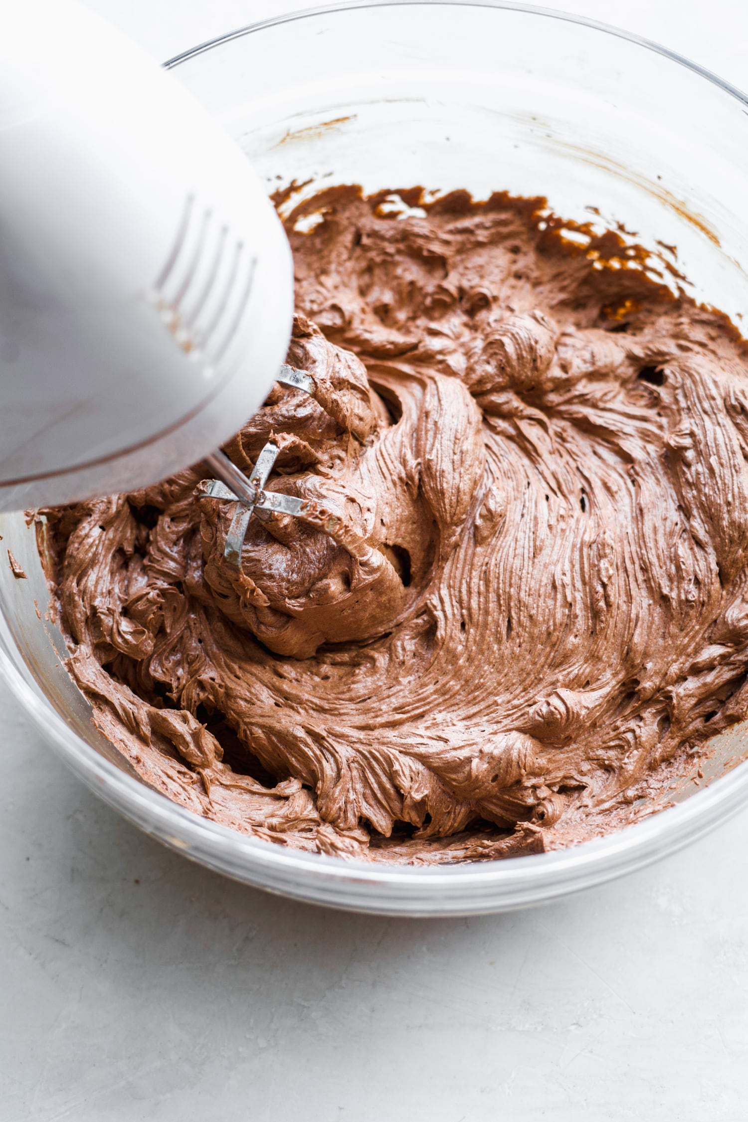 A mixing bowl with vegan frosting being mixed with a hand blender. 
