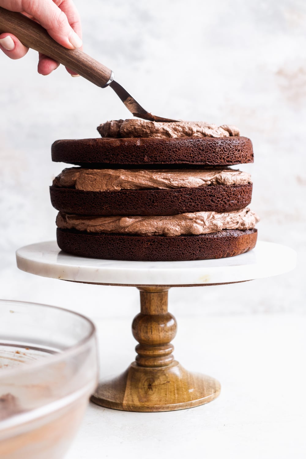 Layers of chocolate cake being stacked and frosted on a cake stand.