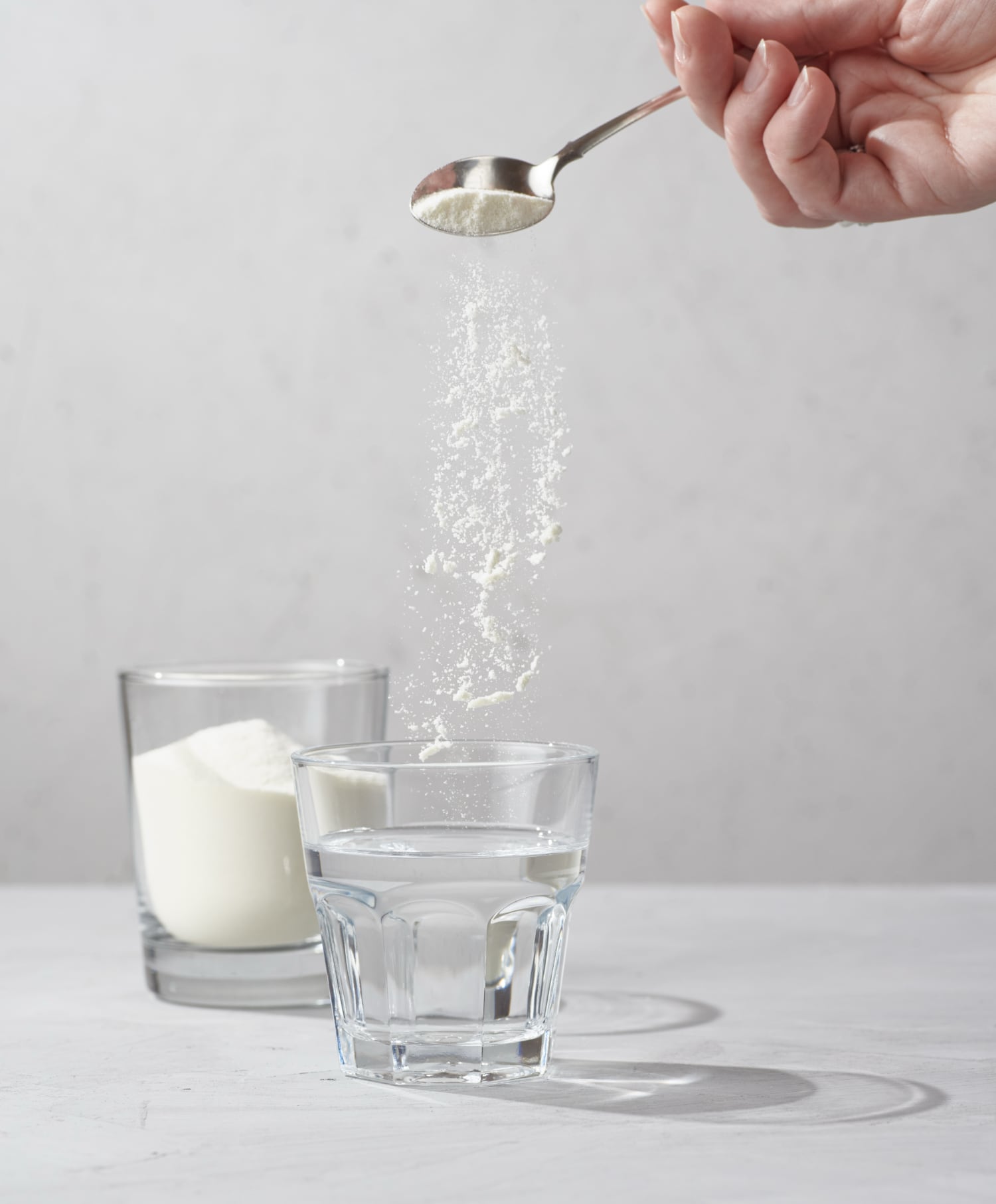 Powdered creatine being sprinkled into a glass of water.