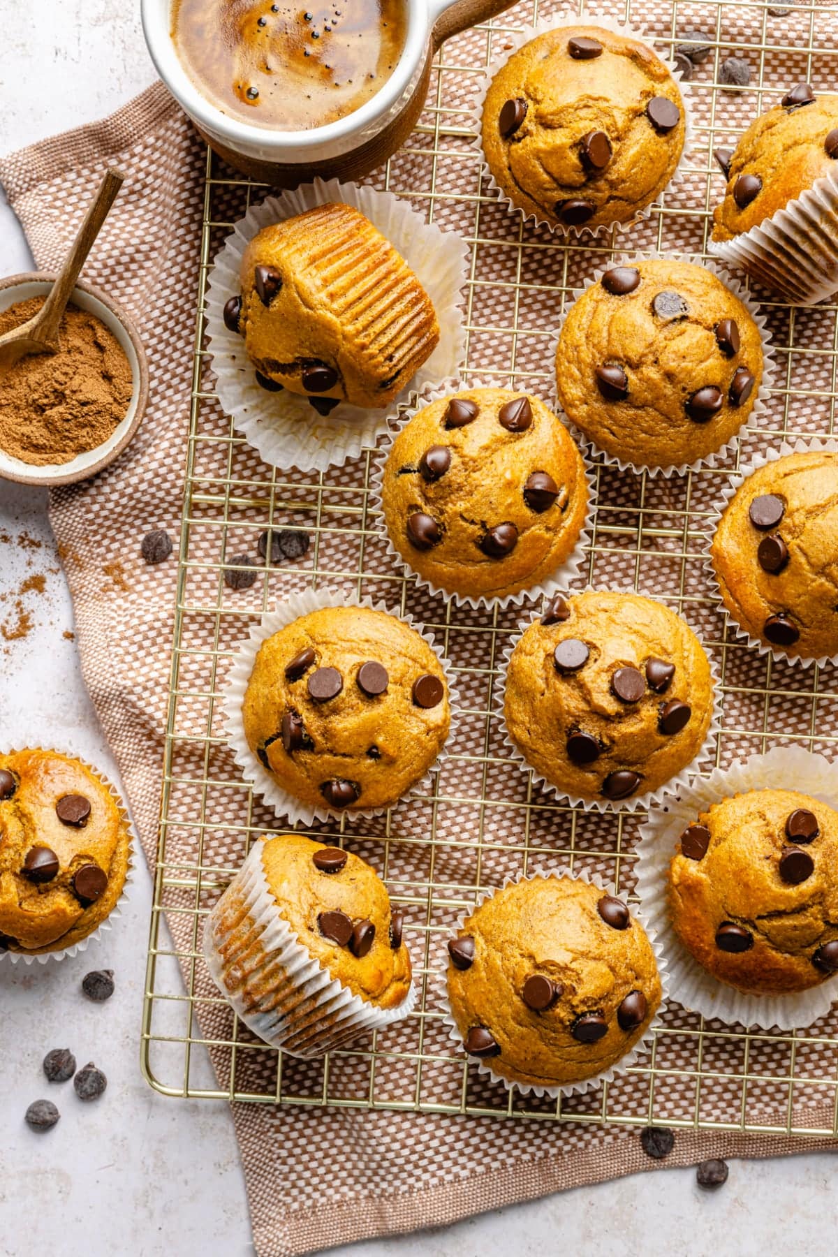 A cooling rack with a dozen baked protein pumpkin muffins cooling and a cup of coffee on the counter.
