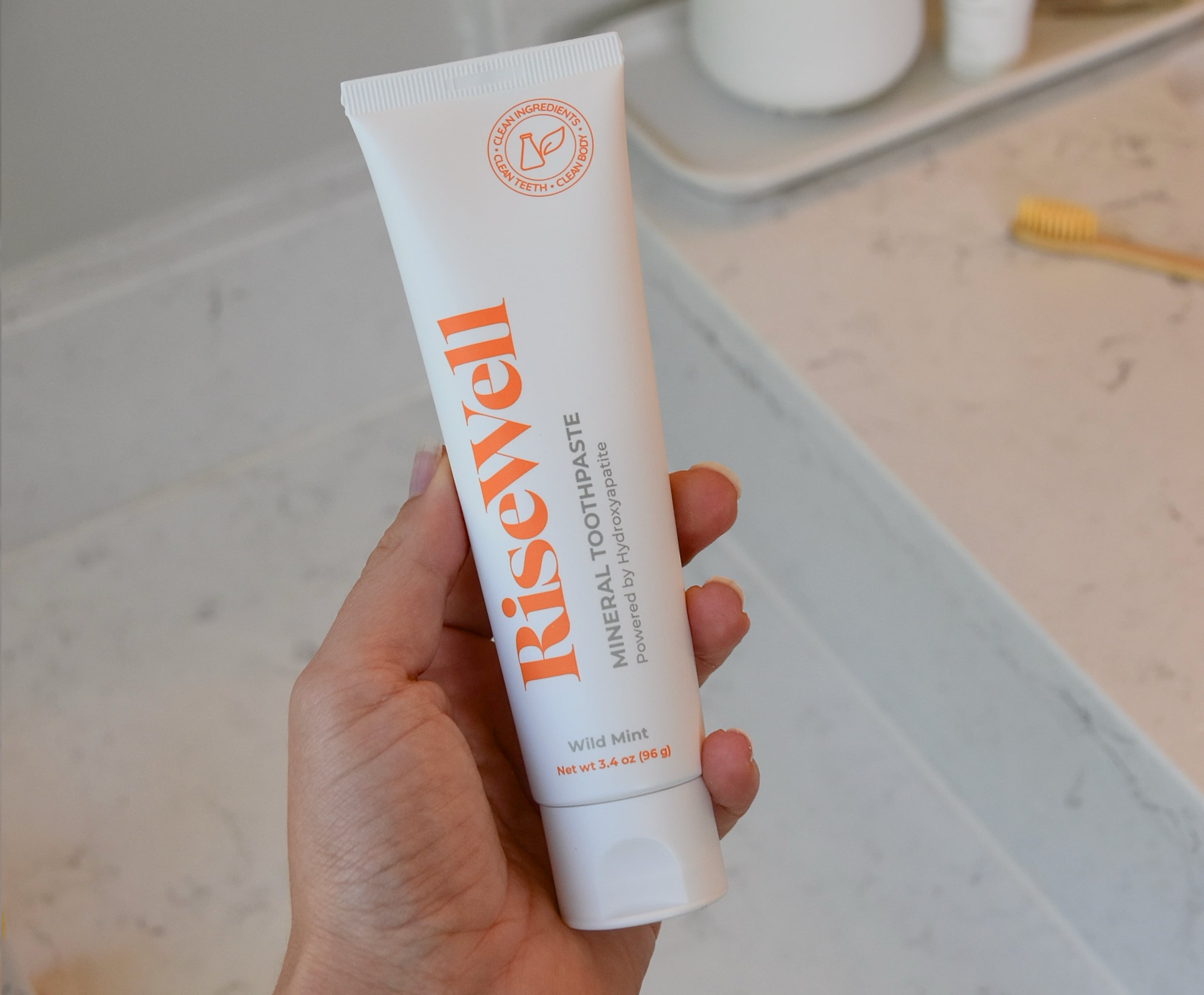 Holding a bottle of the RiseWell Mineral Toothpaste for review.
