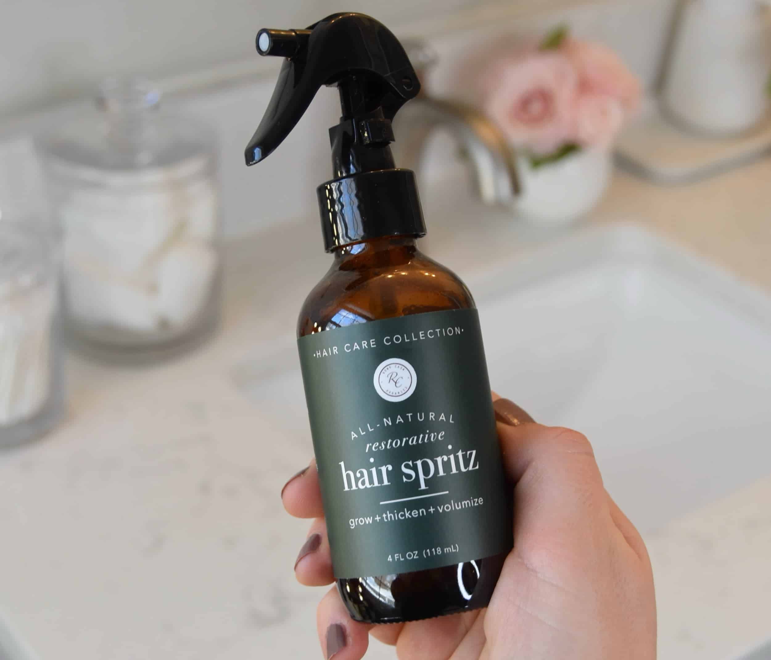 Holding a bottle of the Rowe Casa Organics Hair Spritz in front of the bathroom sink.