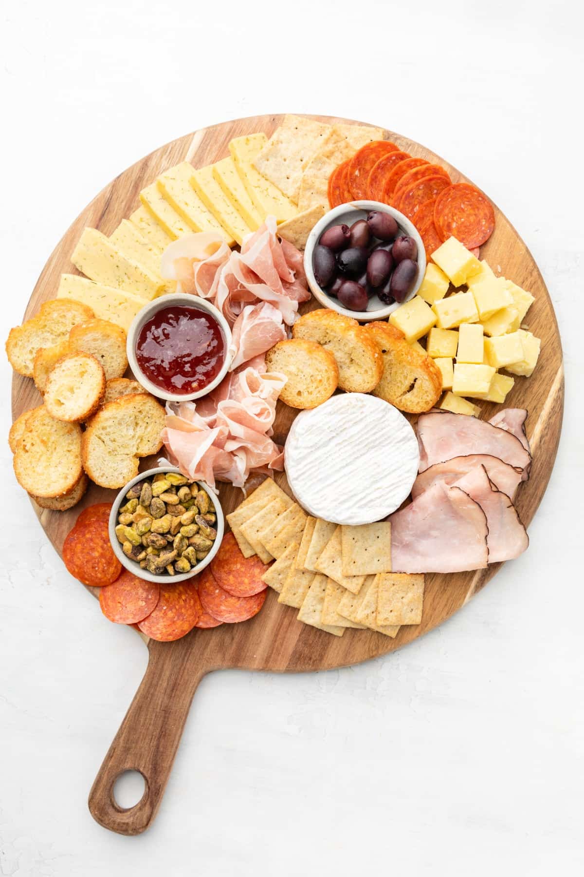 Building a small charcuterie board with accents, cheese, meats, and crackers.
