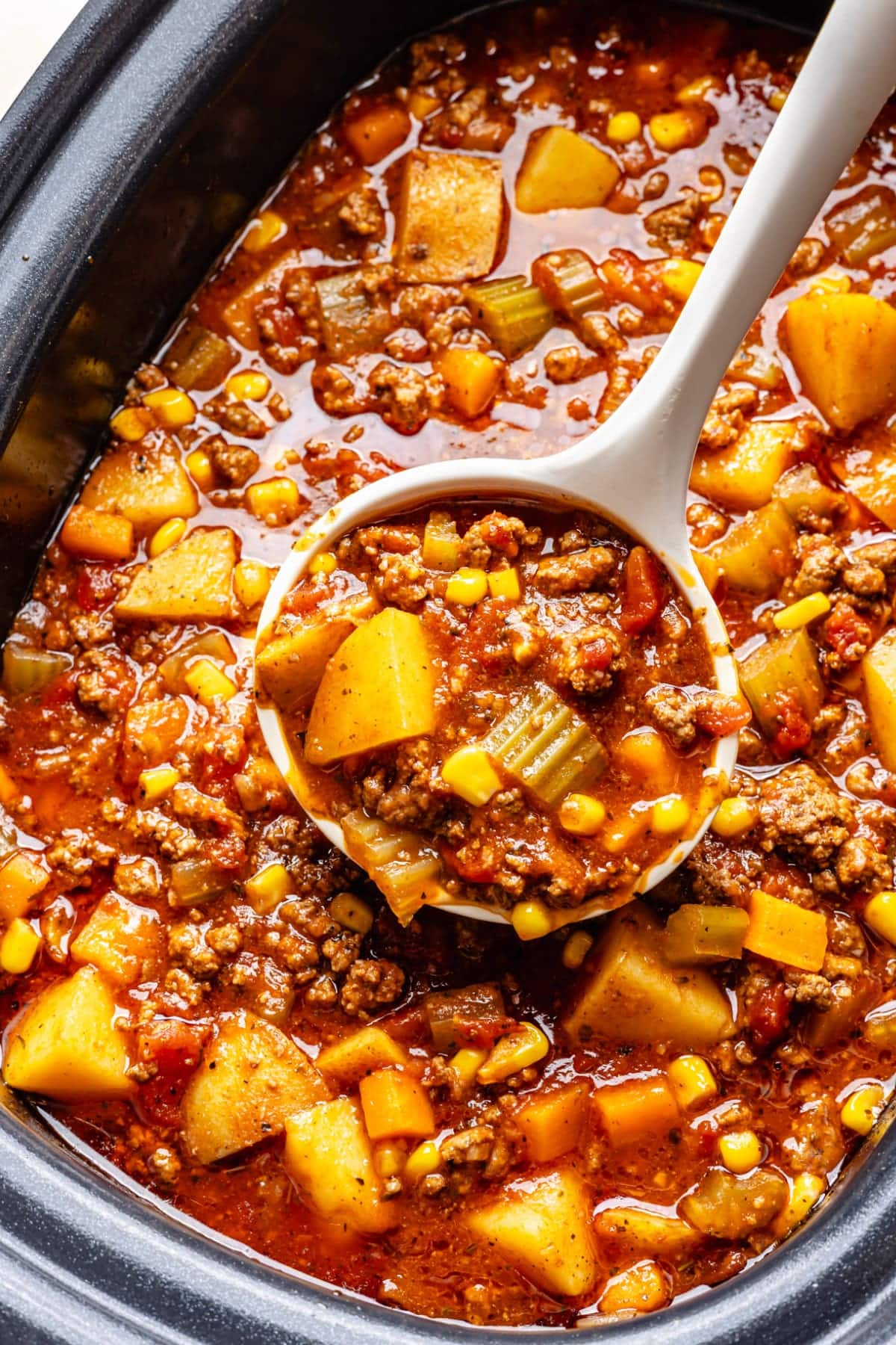 A big batch of hamburger soup in the slow cooker with a large spoon scooping some out to serve in bowls.