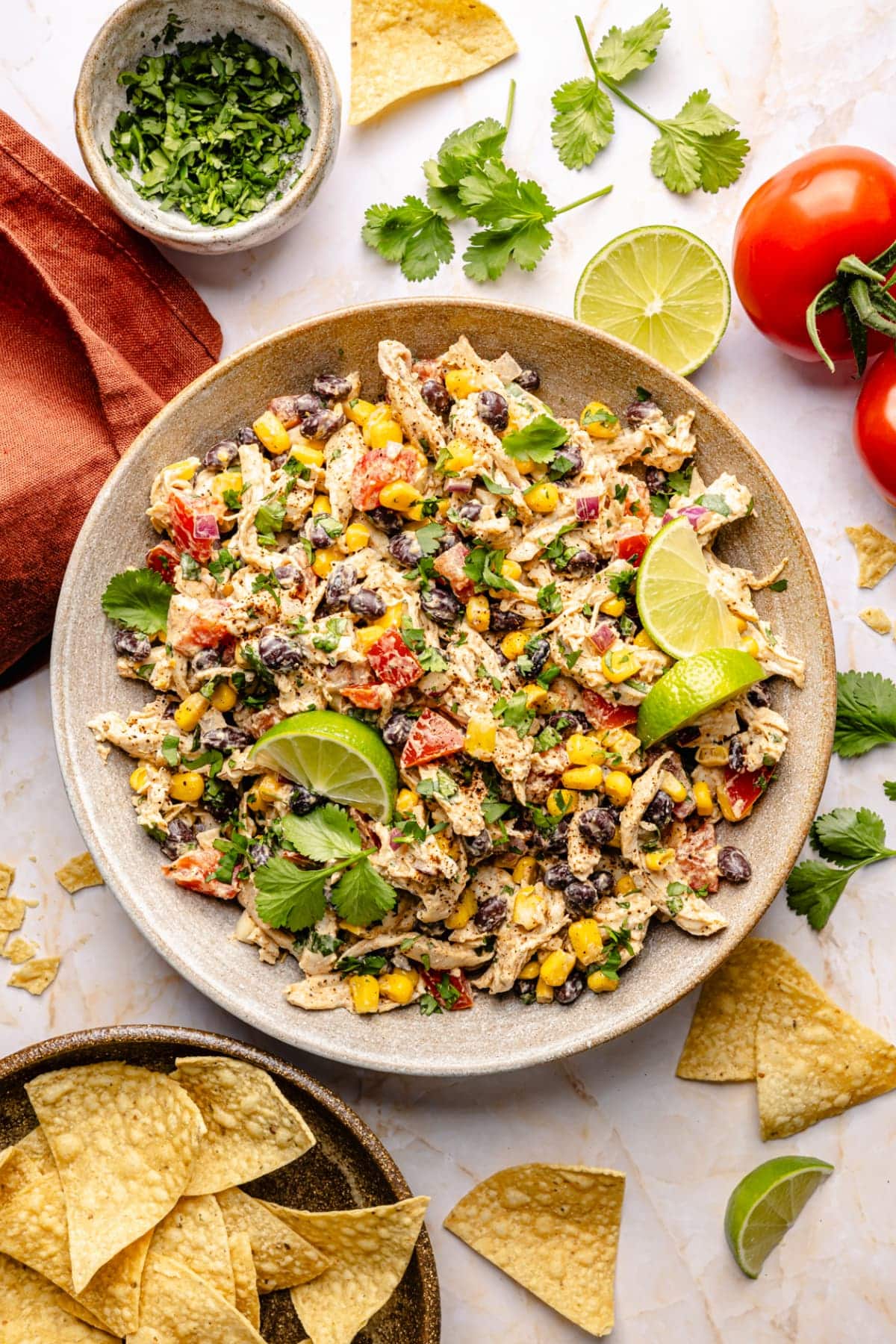 Overhead shot of a large bowl with an entire batch of southwest chicken salad in it surrounded by fresh vegetables, cilantro, and tortilla chips.