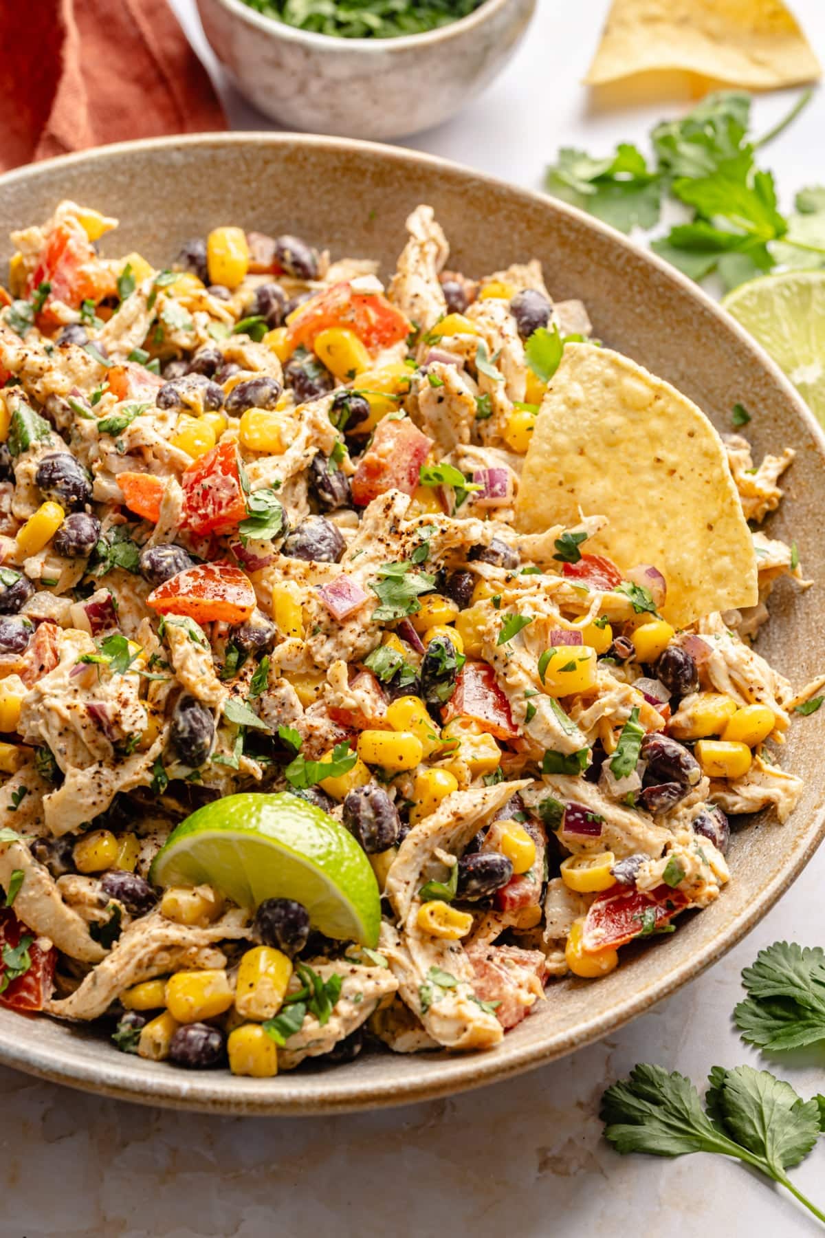 A large bowl with southwest chicken salad in it served with tortilla chips and a lime wedge.