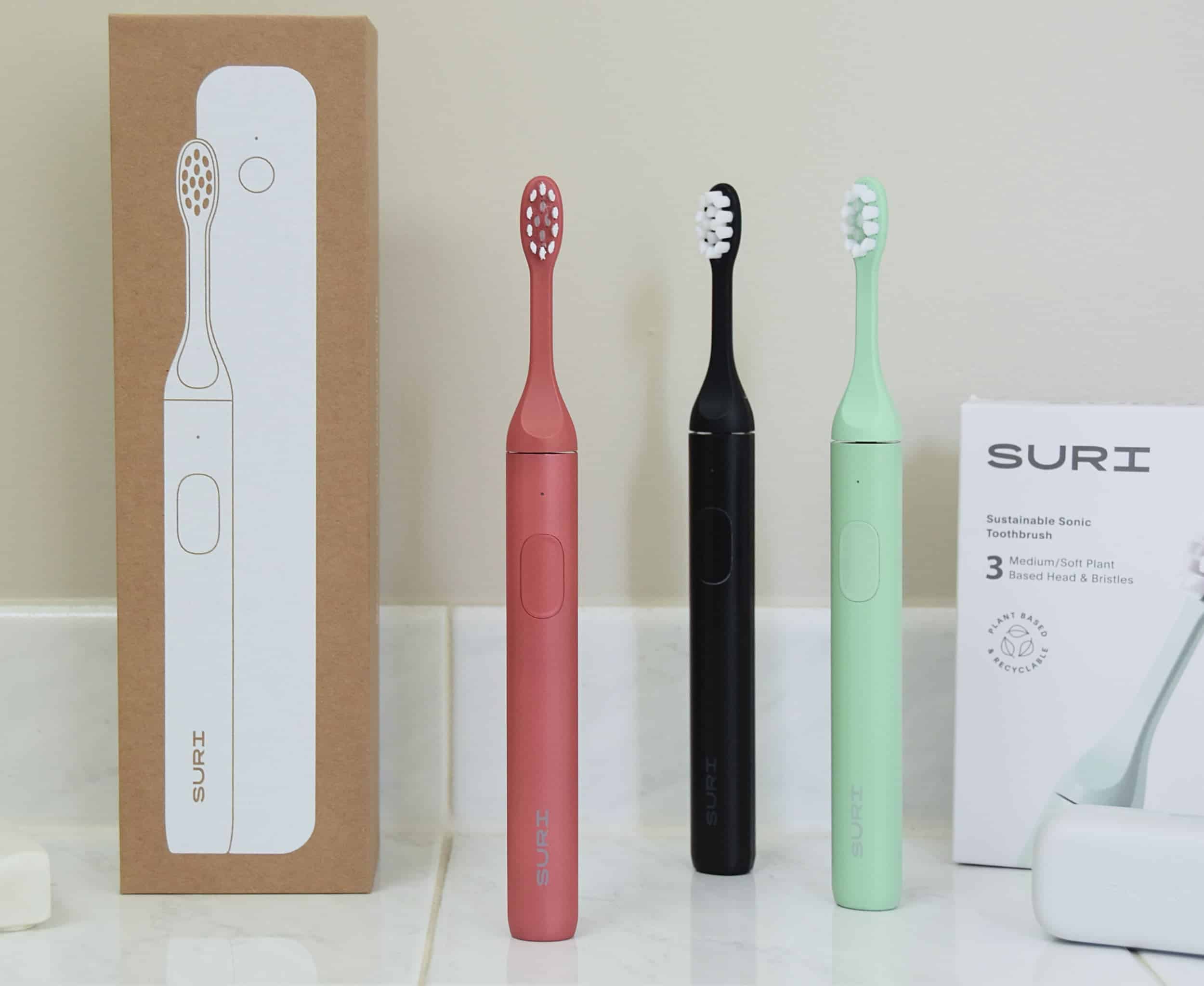 Three toothbrushes on the bathroom counter standing side by side with the packaging.
