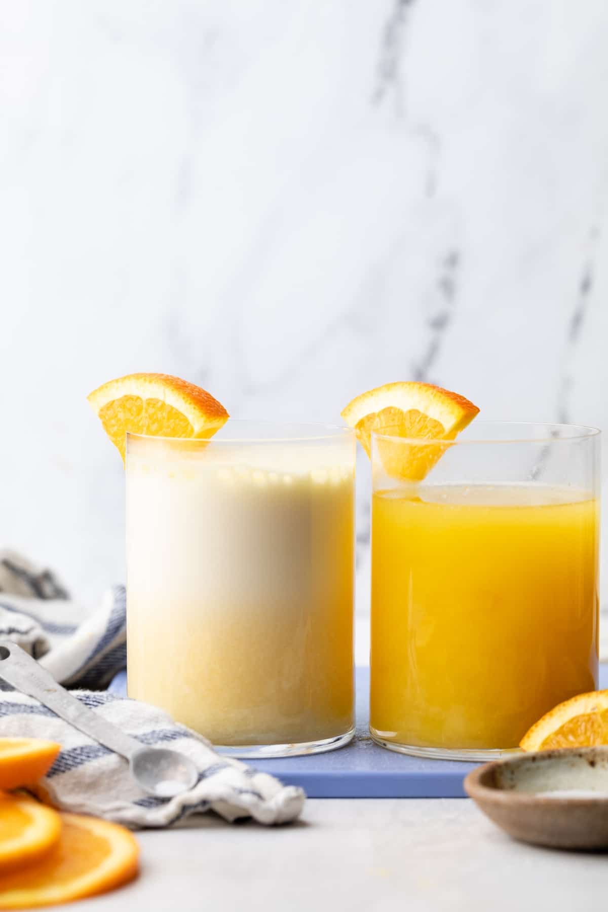 Two glasses with different adrenal cocktail drinks in them and orange slices.