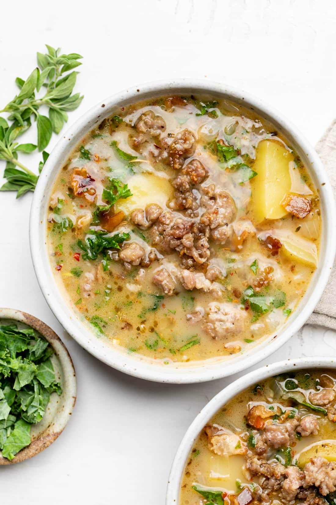 Two bowls of zuppa toscana soup with homemade broth, sausage, and kale in bowls around it.