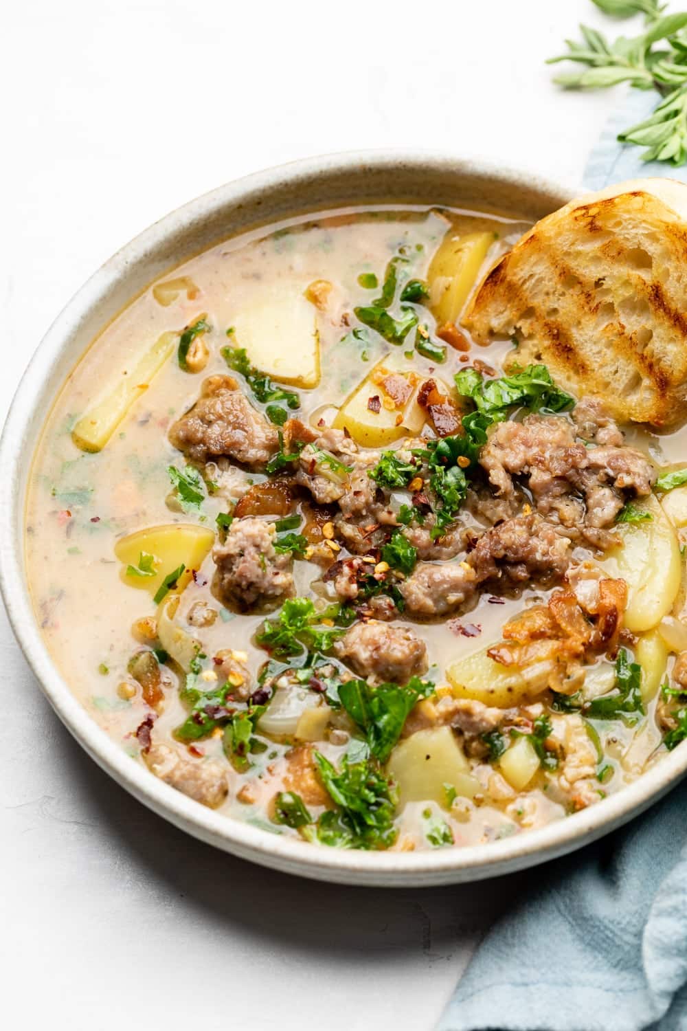A big bowl of zuppa toscana made with healthier ingredients and served with a piece of bread. 